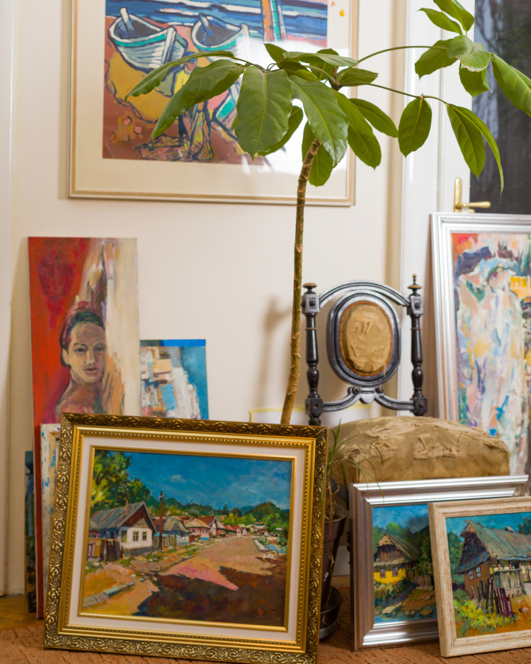 Umetničke slike postavljene na zidu i podu zajedno sa visokom zelenom biljkom